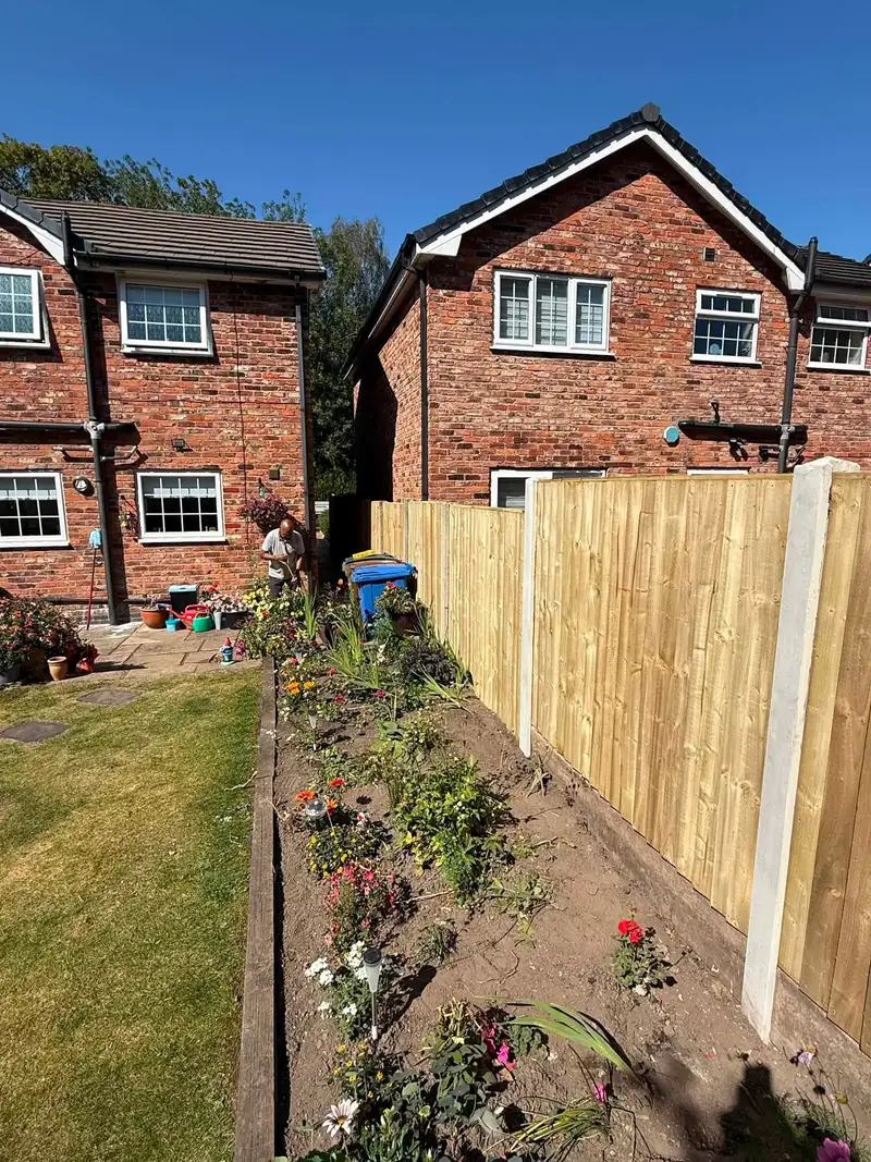 Tall new closeboard fence beside a flower border and lawn at a brick house